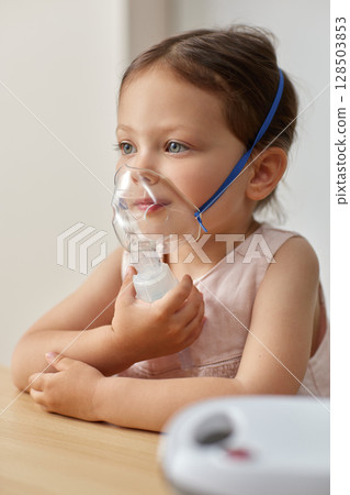 cute little toddler girl inhaling medicine on nebulizer and holding it on her own 128503853