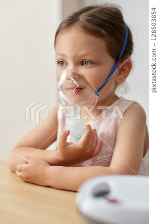 cute little toddler girl inhaling medicine on nebulizer and holding it on her own 128503854