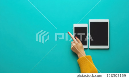 woman pointing at smartphone and tablet on teal background 128505169