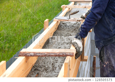 Worker levels concrete in formwork using a trowel Worker levels concrete in formwork using a trowel 128505573