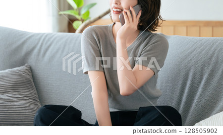 Smiling woman sitting on sofa and talking on smartphone Smiling woman sitting on sofa and talking on smartphone 128505902