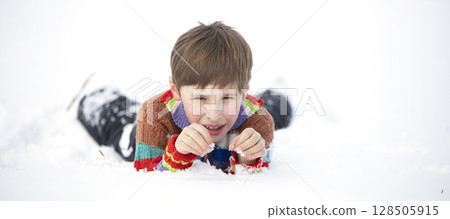 A funny little boy in colorful clothes lies in the snow. A hardened child in winter. A funny little boy in colorful clothes lies in the snow. A hardened child in winter. 128505915