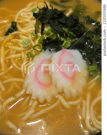 A closeup photo of miso ramen noodle soup, with topping of narutomaki and seaweed.  128505986