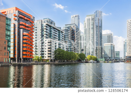 Waterfront skyline of modern glass skyscrapers and apartments reflecting on calm river Waterfront skyline of modern glass skyscrapers and apartments reflecting on calm river 128506174