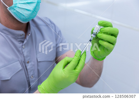 Healthcare Professional Preparing Vaccine Dosage in a Clean Clinical Environment with Green Gloves and a Mask for Patient Safety and Infectious Disease Prevention 128506307