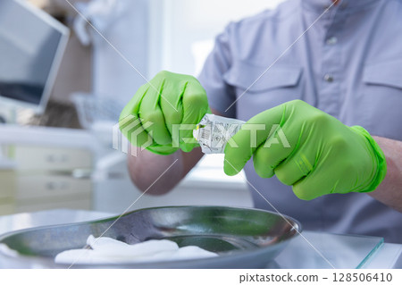 Professional Medical Procedure Demonstration: Practitioner in Green Gloves Handling Medical Supplies in a Clean Clinic Environment 128506410