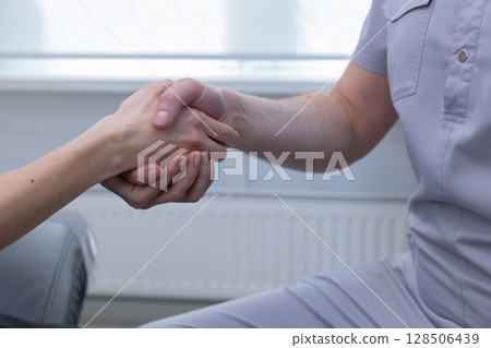 A Warm Gesture of Support: Handshake Between a Medical Professional and a Patient in a Bright Treatment Room A Warm Gesture of Support: Handshake Between a Medical Professional and a Patient in a Bright Treatment Room 128506439