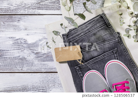 Sustainable still life with jeans with empty label, textile bag and sneakers. Second hand clothing shop. Circular fashion, eco friendly sustainable shopping, thrifty shop concept. Flat lay, copy space Sustainable still life with jeans with empty label, textile bag and sneakers. Second hand clothing shop. Circular fashion, eco friendly sustainable shopping, thrifty shop concept. Flat lay, copy space 128506537