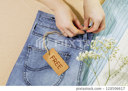 Sustainable life style with female hands holding label with text Free on clothes ready for a garage sale. Circular fashion, eco friendly sustainable shopping, thrifty shop and second hand concept 128506617