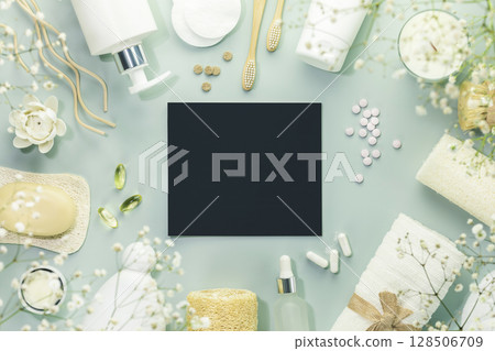 Eco friendly spa relax composition with beauty products, serums, soap, accessories and supplements on blue background with empty chalkboard. Concept of me time, wellness, self care. Copy space 128506709