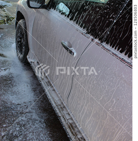 Foam flows down the side of a white large SUV at car washing service  128506803
