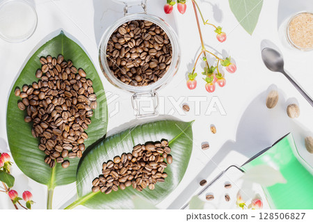 Organic roasted coffee beans on a green leaves, coffee pot and sugar in a glass jars on ivory background with flowers and shadows. Coffee making concept. Natural farm coffee. Flat lay Organic roasted coffee beans on a green leaves, coffee pot and sugar in a glass jars on ivory background with flowers and shadows. Coffee making concept. Natural farm coffee. Flat lay 128506827