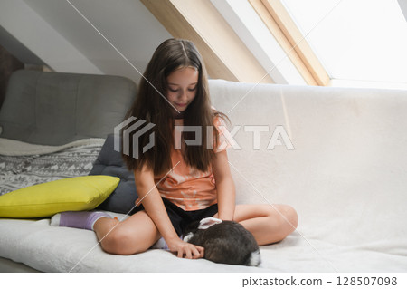 Smiling girl playing with black and white rabbit indoors. Smiling girl playing with black and white rabbit indoors. 128507098