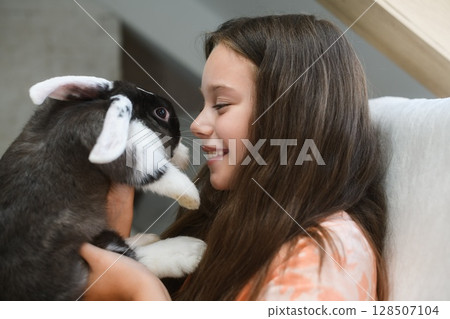 Girl holding fluffy rabbit face to face indoors. Girl holding fluffy rabbit face to face indoors. 128507104
