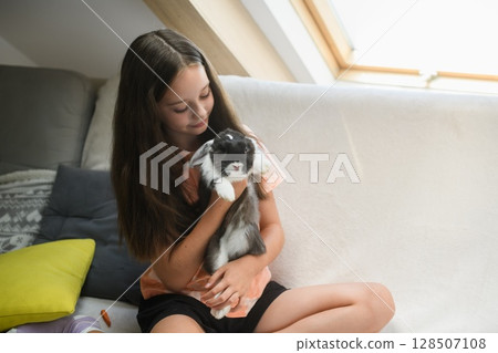 Girl cuddling fluffy rabbit while sitting on sofa. 128507108