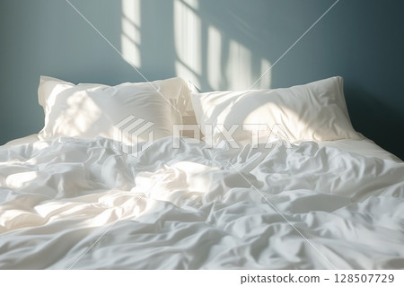 Soft morning sunlight filtering across rumpled bedding, highlighting restful moments and sleep wellness 128507729