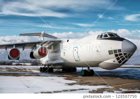 White wide body transport cargo airplane at winter airport on the background of high snow capped mountains 128507750