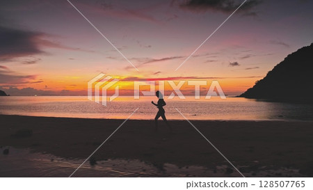 Silhouetted sportswoman running along a picturesque beach in Thailand, embracing the vibrant colors of a stunning sunset while celebrating freedom and a healthy lifestyle Silhouetted sportswoman running along a picturesque beach in Thailand, embracing the vibrant colors of a stunning sunset while celebrating freedom and a healthy lifestyle 128507765