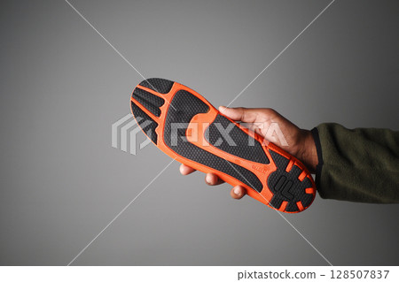 Hand holding an orange and black athletic shoe sole 128507837