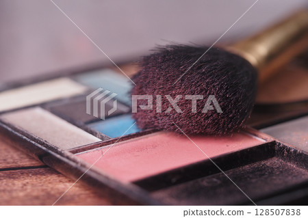 A closeup of a makeup palette and brush on a wooden surface A closeup of a makeup palette and brush on a wooden surface 128507838
