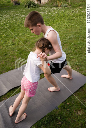 Brother and sister playing outdoors, engaging in playful physical activity on yoga mats. Brother and sister playing outdoors, engaging in playful physical activity on yoga mats. 128508284