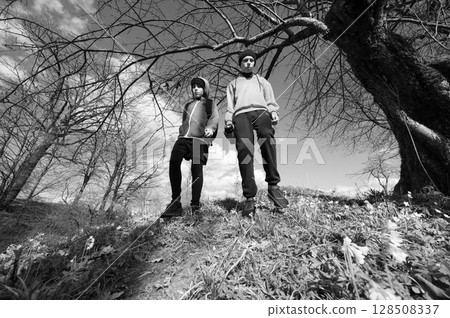 Two young people hiking on a trail, under a large tree. Black and white photography. 128508337