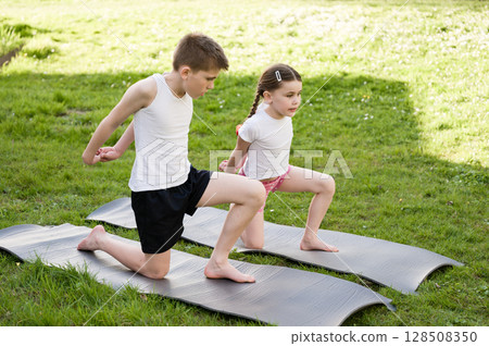 Brother and sister doing yoga stretches outdoors on mats. 128508350