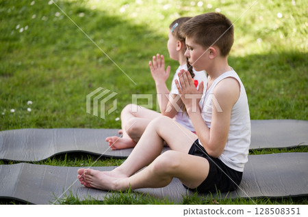 Children practicing yoga outdoors on mats. Peaceful scene of kids meditating in nature. 128508351