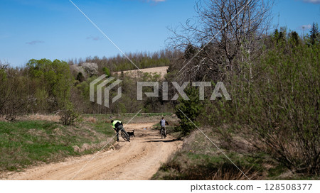 Cyclists and dog on a rural dirt road, enjoying a sunny day outdoors. Cyclists and dog on a rural dirt road, enjoying a sunny day outdoors. 128508377