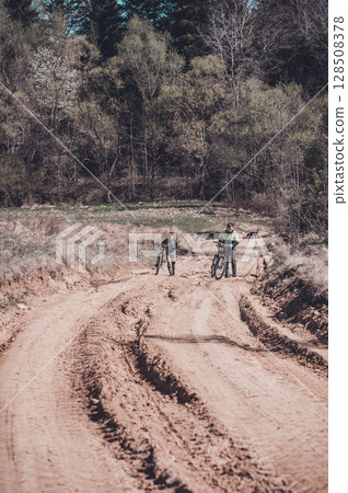 Father and son biking on a dirt road through a forest. A sunny day adventure. 128508378