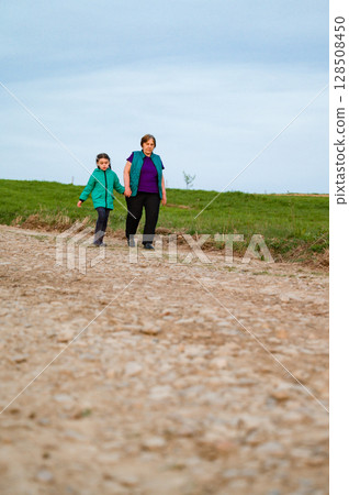 Grandmother and granddaughter holding hands, enjoying a leisurely stroll along a countryside path. Grandmother and granddaughter holding hands, enjoying a leisurely stroll along a countryside path. 128508450