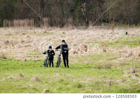 Two boys on bikes enjoying a ride through a grassy field, surrounded by trees. Two boys on bikes enjoying a ride through a grassy field, surrounded by trees. 128508503