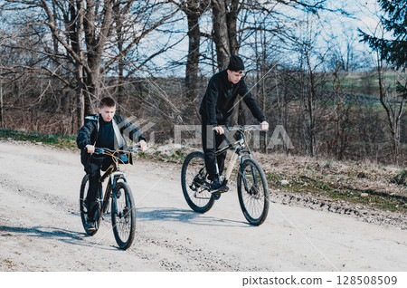 Two boys cycling down a dirt road, enjoying a sunny day outdoors. A peaceful countryside scene. 128508509