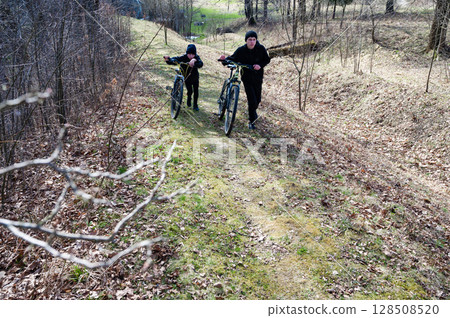 Two boys walk their bikes along a wooded path, enjoying a spring day outdoors. Two boys walk their bikes along a wooded path, enjoying a spring day outdoors. 128508520