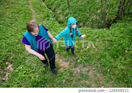 Grandmother and granddaughter enjoy a spring walk in the woods, holding hands. 128508521