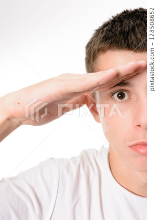 Young man looking into the distance, hand shielding his eyes from the sun. 128508652