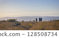 Figures of men with guns and binoculars against the background of the morning hilly landscape. 128508734