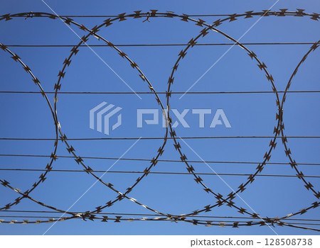 Flat security barrier made of reinforced barbed tape on the fence. 128508738