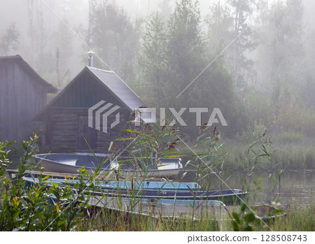 Rowboats on the shore of body of water in the morning fog. 128508743