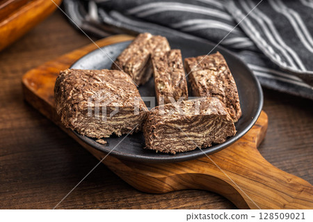 Halva with cocoa. Sweet oriental dessert on plate on wooden table. 128509021