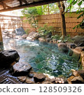 An open-air bath with a tranquil atmosphere, surrounded by bamboo fences and natural trees. 128509326