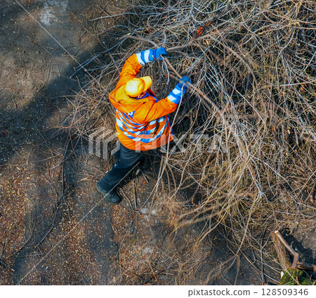 Dnipro, Ukraine - March 20, 2024: City municipal service worker remove and saw cut tree branches in the courtyard of apartment building. View from above. 128509346
