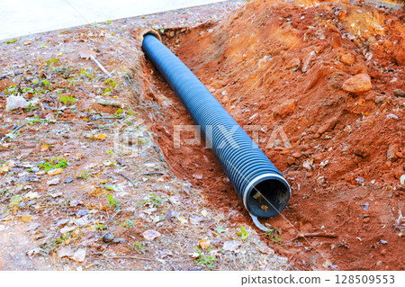 Excavation site with newly installed drainage pipe positioned in trench during construction work Excavation site with newly installed drainage pipe positioned in trench during construction work 128509553