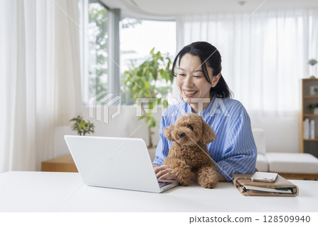 Middle-aged woman working on a laptop and her pet dog, working from home image 128509940