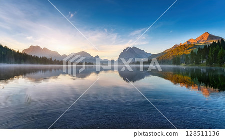 tranquil lake reflecting misty mountains at sunrise, symbolizing calm and balance 128511136