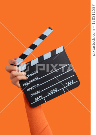 Womans hand holding clapperboard on an orange background Womans hand holding clapperboard on an orange background 128511587