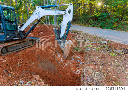 Heavy machinery digs into earth trench for installed drainage pipe 128511804