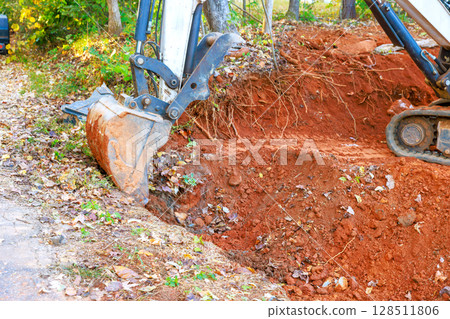 Large excavator digs trench in rural setting, for installed drainage pipe amidst construction site 128511806