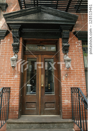 An old wooden double door with glass panels is framed by black decorative columns and brick walls. Lantern-style lights and a classic pediment complete the historic entrance. An old wooden double door with glass panels is framed by black decorative columns and brick walls. Lantern-style lights and a classic pediment complete the historic entrance. 128513461