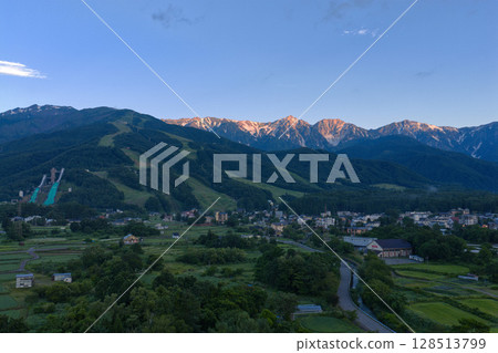 Morning glow of the Hakuba Sanzan mountains and Hakuba village in summer Hakuba village, Nagano prefecture (aerial photography by drone) Morning glow of the Hakuba Sanzan mountains and Hakuba village in summer Hakuba village, Nagano prefecture (aerial photography by drone) 128513799